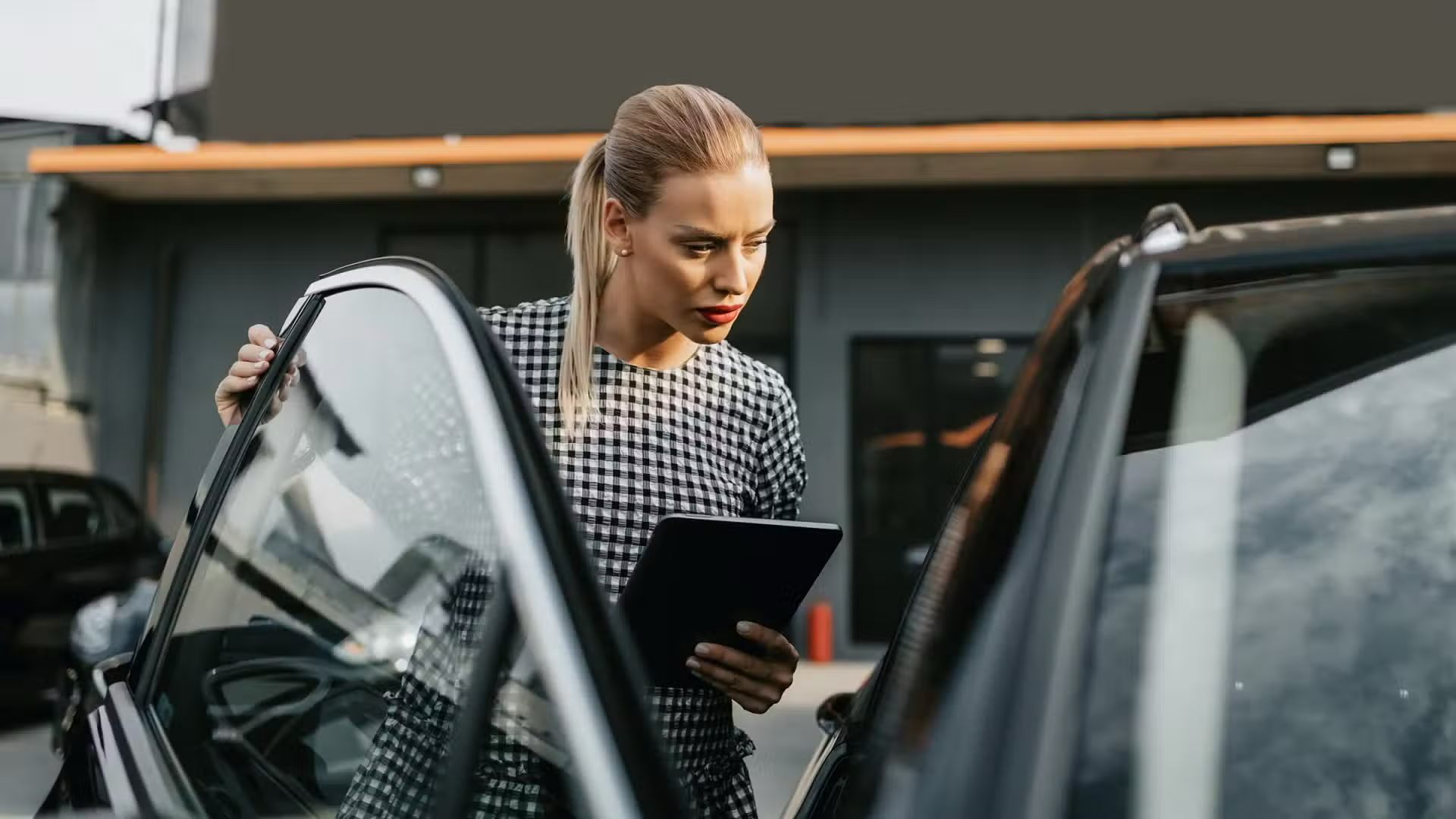 A used-car buyer checking a vehicle's details on a tablet beside the car at a dealership